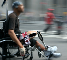 Black man with leg prosthesis using wheelchair while crowd blurs behind him